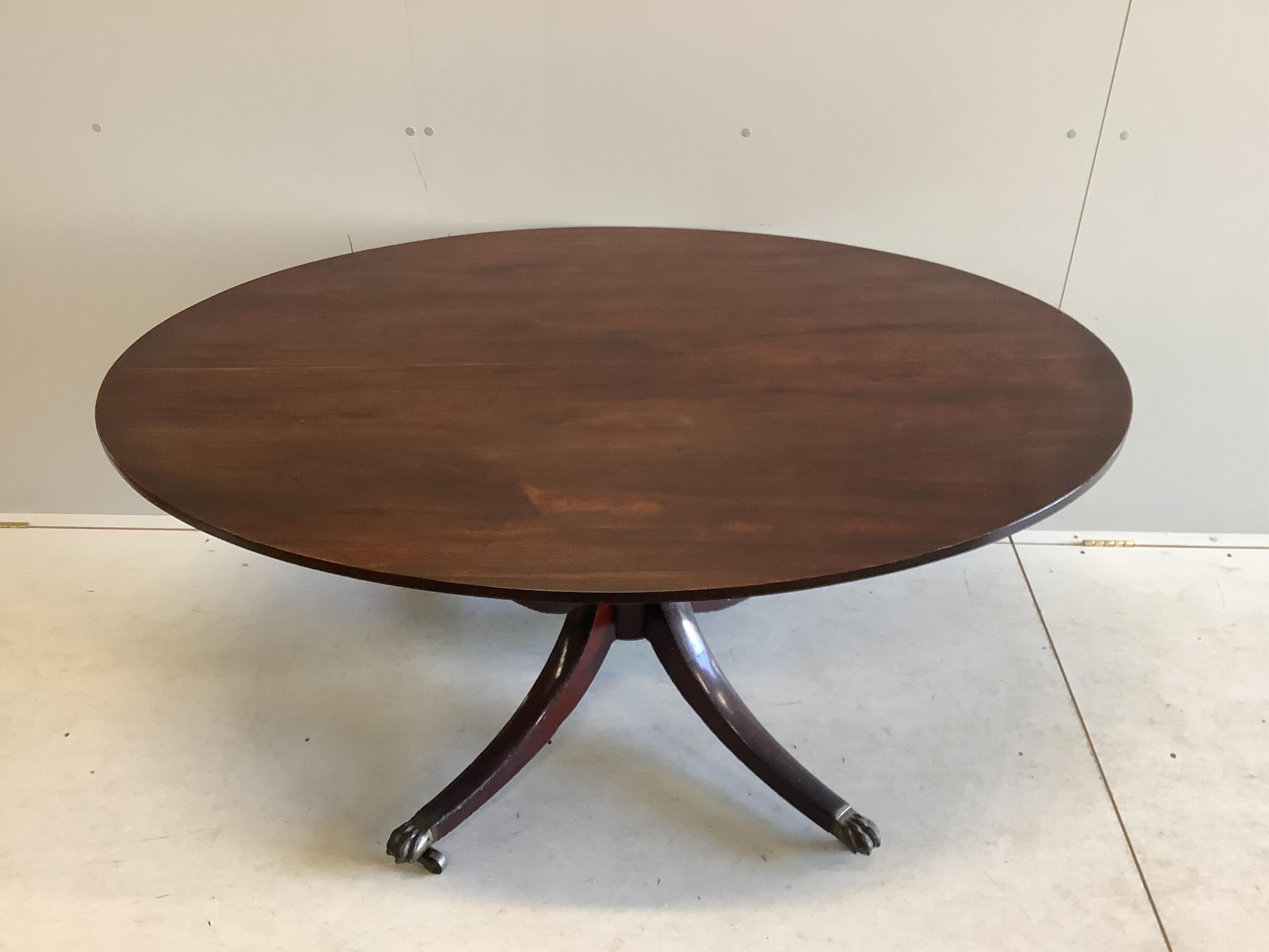 A George III mahogany oval pedestal dining table with brass claw feet, width 152cm, depth 105cm, height 71cm, together with a set of six Regency mahogany sabre leg dining chairs. Condition - fair to good